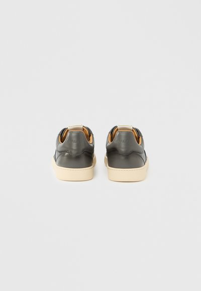 Μαύρα δερμάτινα αθλητικά παπούτσια με μπεζ λαστιχένιες σόλες, με λεία υφή και μινιμαλιστικό σχέδιο. Πίσω θηλιά για εύκολη εφαρμογή.