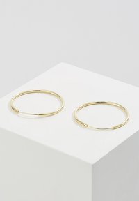 Pendientes de aro de oro con un acabado liso y pulido. Diseño delgado con un cierre seguro, exhibidos en un pedestal blanco.