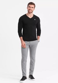 Musta pitkäähihaista v-pääntie paitaa, vaaleanharmaat slim-fit housut, mustat lenkkikengät ja kello, jossa on pieni logo paidassa.