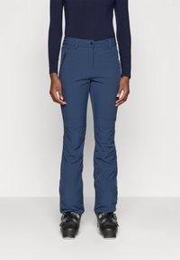 Mørkeblå skibukser med slim fit, med en glidelås lomme, buede sømmer og et behagelig stretchy stoff. Brukt med svarte skistøvler.