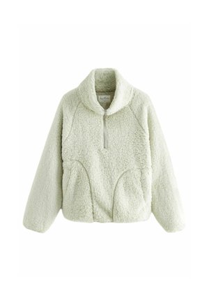 Personne portant une veste zippée duveteuse vert clair avec les mains dans les poches, montrant la texture et le détail de la fermeture éclair avant.
