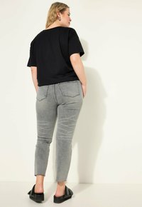 Camisa negra de manga corta combinada con jeans ajustados grises, con detalles desgastados y dobladillos deshilachados, y zapatos negros de plataforma de tipo slip-on.