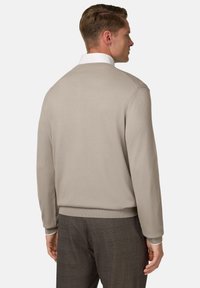 Pull en tricot beige avec des poignets et un ourlet côtelés, présentant un col rond classique et une texture lisse. Porté par-dessus un pantalon à carreaux.