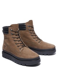 Bottes montantes en cuir marron à lacets, avec col rembourré noir, semelles épaisses en caoutchouc noir et logo en relief discret sur le côté.