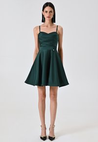 Robe en satin verte avec un corsage ajusté, décolleté en cœur et jupe évasée. Dispose de fines bretelles et d'un petit accent métallique.