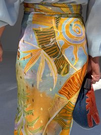 Colorful, patterned skirt with leaves and swirls; person holds a textured blue and red purse, standing in a bright, neutral-toned space.