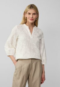 Witte geborduurde blouse met een v-hals, driekwart mouwen en ingewikkelde bloemmotieven, gecombineerd met beige hoge taillebroek.