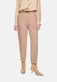 Beige maßgeschneiderte Hose mit schmal zulaufendem Bein, aufgeschlagenen Säumen und einer glatten Textur, kombiniert mit einer beigen Satinbluse und nude-farbenen spitzen Pumps.