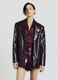 Glänzender dunkelburgunderfarbener Blazer mit scharfen Revers, über einem passenden Hemd getragen. Glänzende, mit Pailletten besetzte burgunderfarbene Shorts runden den Look ab.