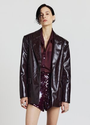 Blazer bordeaux foncé brillant avec des revers nets, superposé à une chemise assortie. Un short bordeaux scintillant et pailleté complète le look.