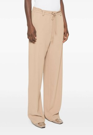 Donna che indossa pantaloni beige a gamba larga con coulisse in vita e scarpe beige appuntite con fibbia decorativa.