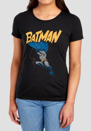 Woman wearing a black t-shirt with a colorful Batman graphic and logo on the front, paired with light blue jeans.