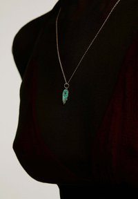 Collar de cadena de plata con un colgante de mano de turquesa que presenta un diseño de ojo, exhibido sobre un fondo negro.