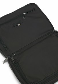 Custodia nera per laptop con un'esterno liscio, compartimenti con doppia cerniera e un'etichetta in tessuto. L'interno presenta un rivestimento morbido e nessun ulteriore motivo.