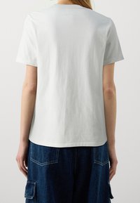 Vit bomullströja med korta ärmar, rund halsringning och avslappnad passform, tillsammans med mörkblå denimbyxor med cargofickor.