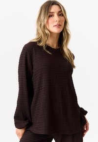 Dark brown long-sleeve top with a textured, crinkled fabric and a relaxed fit. Round neck and slightly loose sleeves.