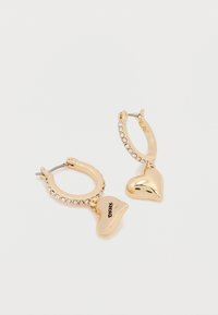 Zlaté kruhové náušnice s lesklým srdcom a príveskom s vyrytým textom, ozdobené čírymi kamienkami na obruči.