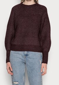 Pull en maille bordeaux avec une texture côtelée, encolure ronde et épaules tombantes, associé à un jean bleu clair délavé.
