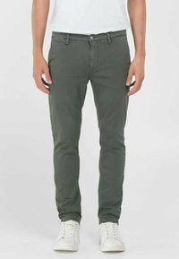 Pantalons chino en coton vert avec une coupe slim, poches avant et fermeture à bouton unique, assortis à des baskets blanches.