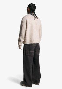 Beige, flauschiger Pullover mit Rundhalsausschnitt, kombiniert mit lockeren, dunklen Jeans aus Denim mit zwei Gesäßtaschen und sichtbaren Nähten.