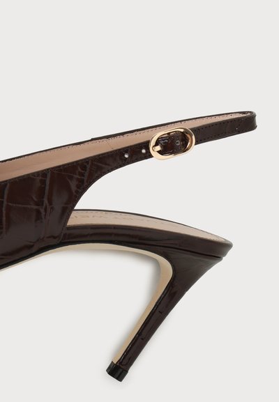 Escarpin slingback en cuir verni marron avec talon haut, boucle dorée et bout pointu, vue de profil sur fond gris.