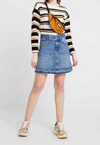 Džínová sukně s roztrhaným lemem, s vysokým pasem a modrou barvou. V kombinaci s černým a žlutým pruhovaným svetrem a pohodlnými teniskami.