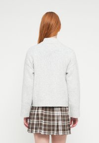 Jasnoszary sweter z dzianiny z prążkowanym wykończeniem na dole i przy kołnierzu, zestawiony z brązowo-białą plisowaną spódnicą w kratę.