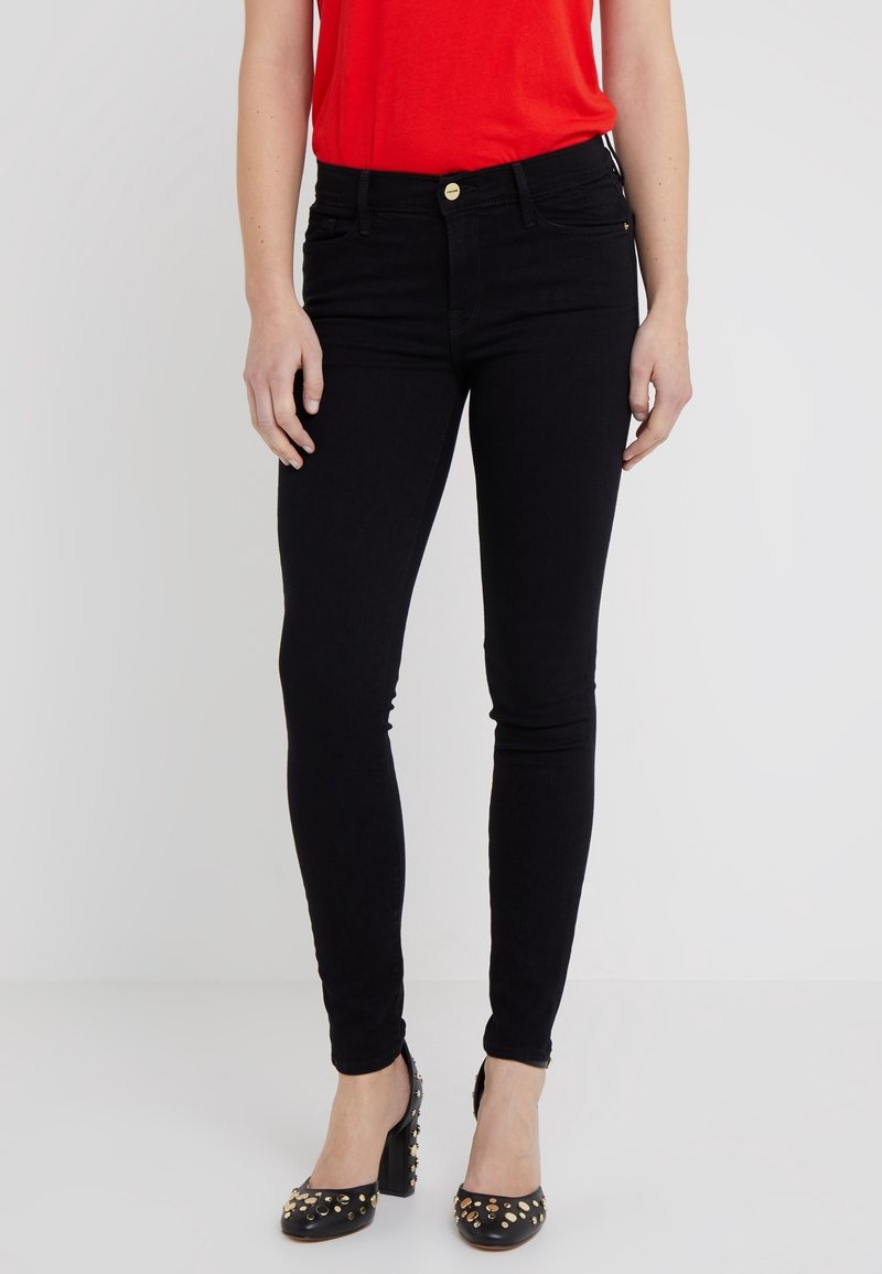 Black skinny jeans made of denim with a fitted design, featuring a gold button closure and side pockets, paired with black studded heels.