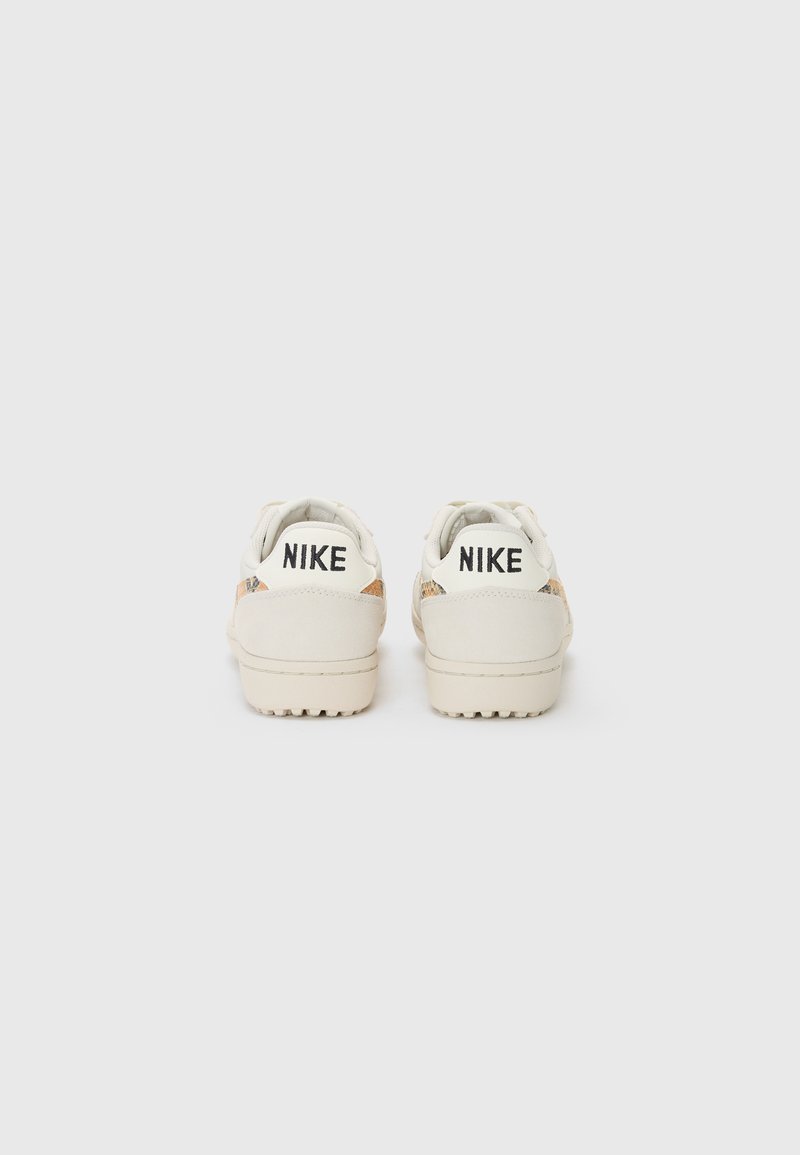 Baskets Nike blanches avec une finition en cuir lisse, présentant un panneau arrière texturé et un logo noir sur le talon, un design basse de type low-top et une semelle en caoutchouc.
