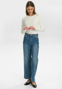 Höga blå denimjeans med vida ben, med en texturerad midjeband. Kombinerat med en figurnära långärmad vit topp och svarta skor.