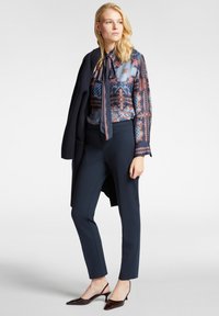 Merenkeulat yhdistettynä kuvioituun siniseen ja marooni puseroon, jossa on kauluskori, täydentäen asua tummalla takilla ja kiiltävillä teräväkärkisillä kengillä.