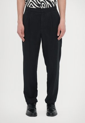 Black trousers with a relaxed fit, featuring front pleats and a smooth texture. Paired with black shoes for a cohesive look.