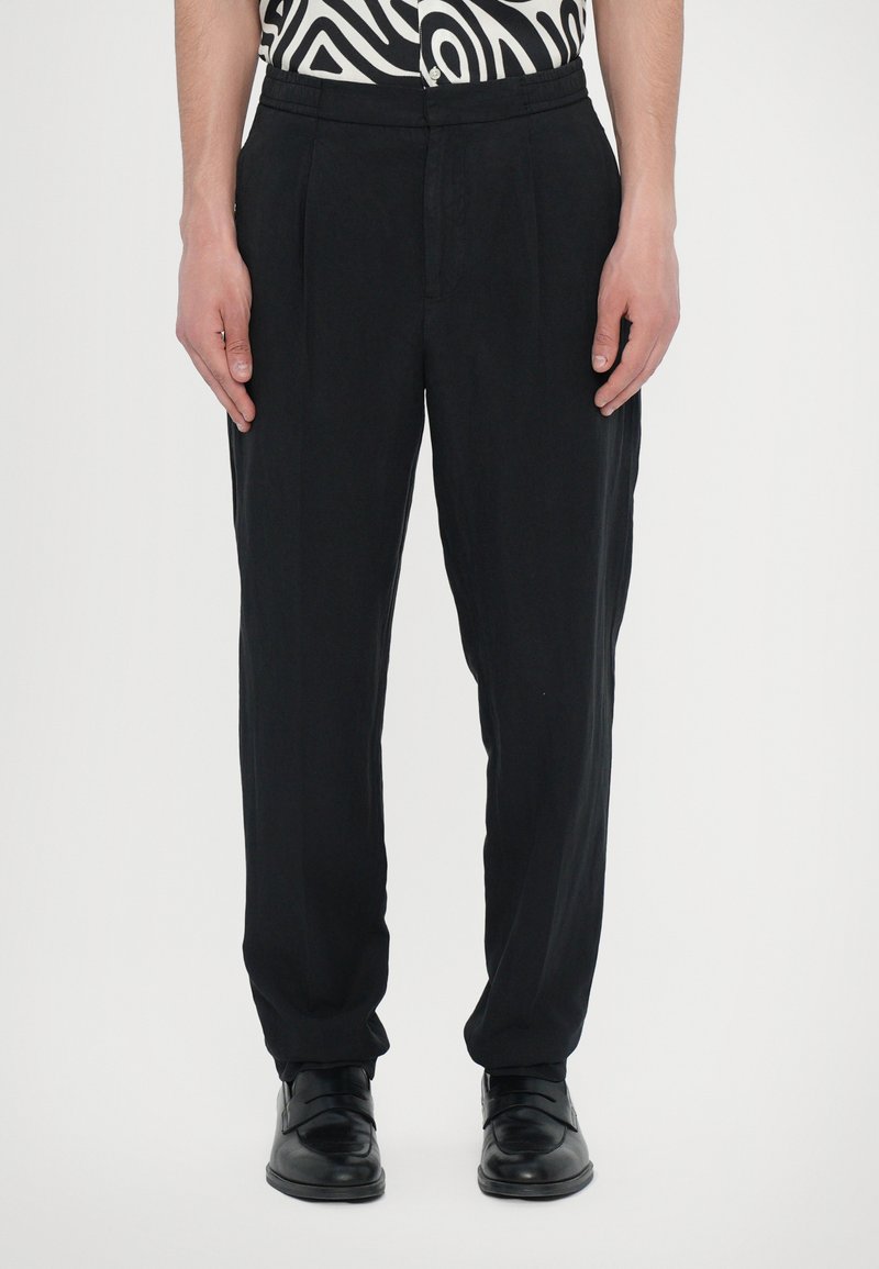 Black trousers with a relaxed fit, featuring front pleats and a smooth texture. Paired with black shoes for a cohesive look.