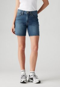 Szorty jeansowe w ciemnym odcieniu niebieskiego z wysokim stanem, postrzępionym dołem i fasonem z pięcioma kieszeniami, zestawione ze srebrnymi trampkami i białymi skarpetkami do kostek.