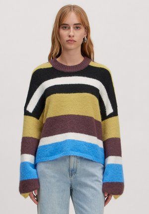 Gestreepte trui in groen, zwart, wit, bruin en blauw. Gemaakt van een fuzzy materiaal met een ronde nek en oversized mouwen. Gedragen met lichte jeans.
