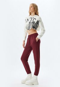 Kornet hvid hoodie med NYC grafik, parret med maroon joggingbukser med elastisk talje og manchetter, iført hvide chunky støvler.