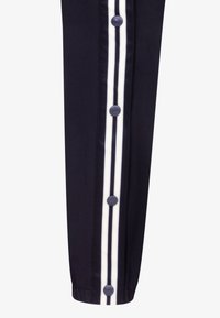 Pantalones marinos con cierres de botón en los laterales y acentos de raya blanca. Presentan un tejido suave y un dobladillo con puño ajustado.