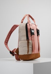 Reppu, jossa on beige tikattu kangasrunko, vaaleanpunaiset hihnat ja ruskea mokkanahkapohja. Varustettu vetoketjulla ja säädettävillä hihnoilla.