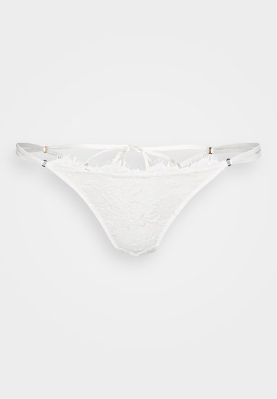 Tanga de encaje blanco con un delicado patrón floral, tirantes finos y pequeños acentos en dorado. Presenta un diseño con cortes.
