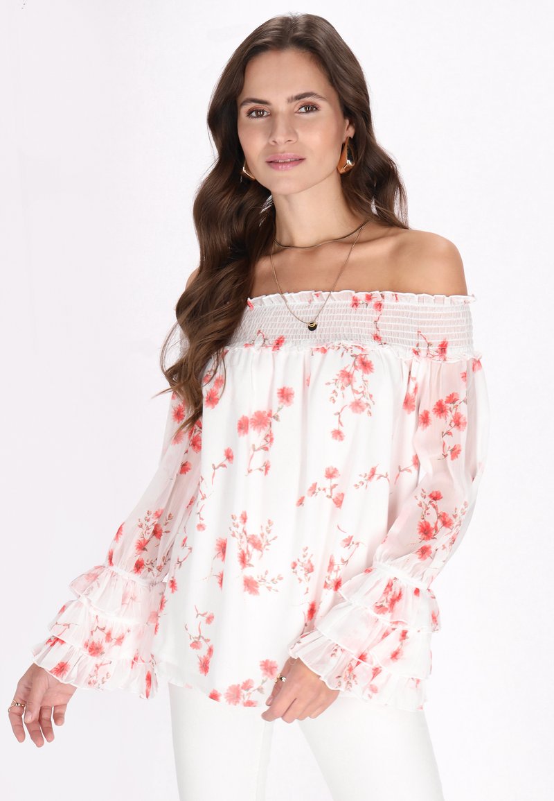Off-shoulder bluse i gennemsigtigt hvidt stof med rødt blomsterprint, der har smocket halsudskæring og flæser ved ærmerne.