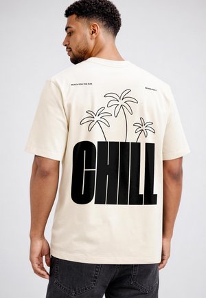 Mann trägt ein hellbeiges T-Shirt mit schwarzen Palmenumrissen und großem, fett gedrucktem Text mit der Aufschrift "CHILL" auf dem Rücken.