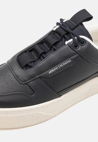 Svart lær sneaker med teksturert overflate, elastiske snorer og en kontrastfarget kremfarget såle med et subtilt spraglet mønster.