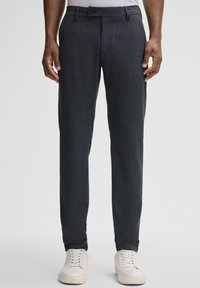 Dunkelgraue maßgeschneiderte Hose aus strukturiertem Stoff, mit schmaler Passform, Gürtelschlaufen und Knopfverschluss. Kombiniert mit weißen Sneakers.