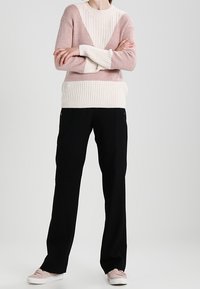 Pull en rose et crème, texture côtelée avec un motif en blocs ; associé à un pantalon noir et des baskets rose clair.