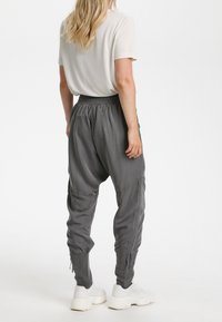 Grå, löst sittande byxor med elastisk midja, avsmalnande ben och sidofickor, ihop med en enkel vit t-shirt och vita sneakers.