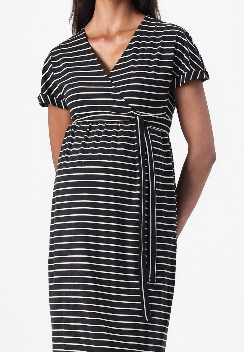 Femme portant une robe de maternité rayée horizontale noire et blanche avec des manches courtes et un décolleté en V cache-cœur noué à la taille.