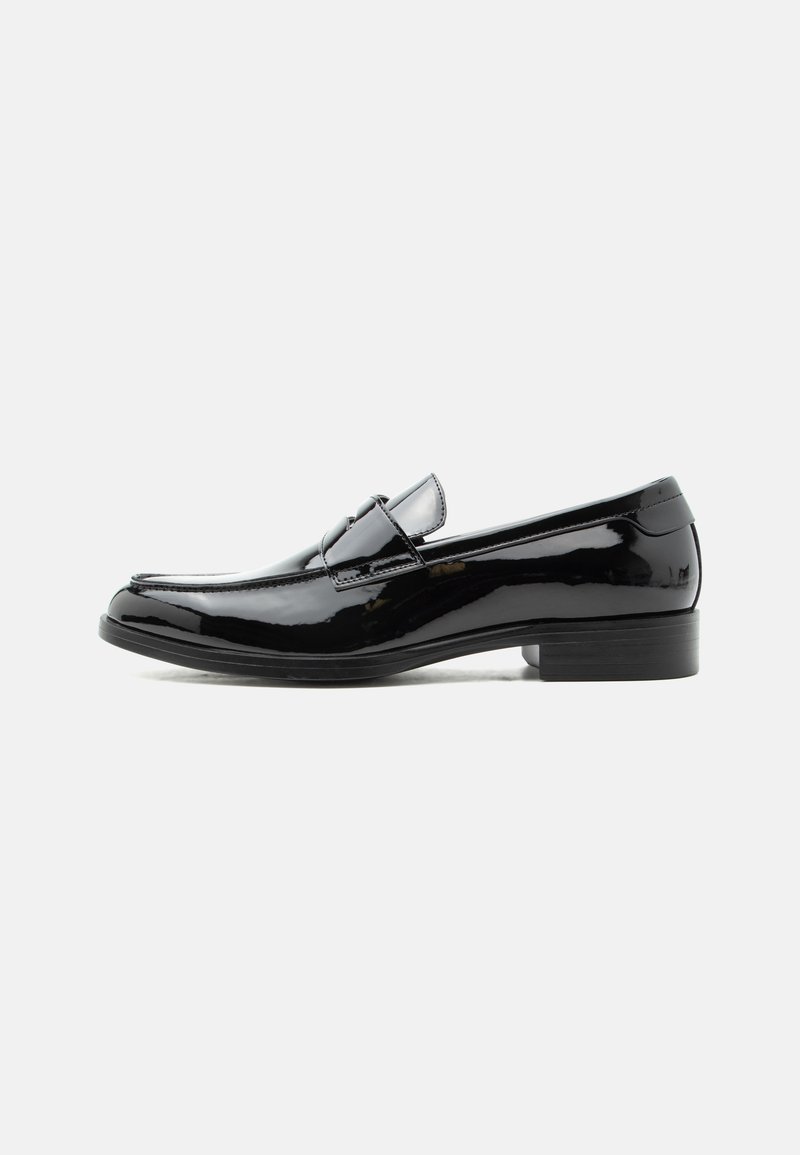 Mocassin pour homme en cuir verni noir avec talon bas, bout arrondi, et détail de bride sur le dessus, sur fond blanc.