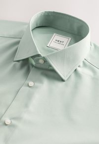 Myntegrøn bomuldsskjorte med klassisk krave, med hvid label og fire hvide knapper, glat tekstur og skræddersyet pasform.