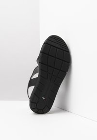 Black sandal with rubber sole, textured tread, and smooth straps. Notable details include circular logo and Italian flag accent.