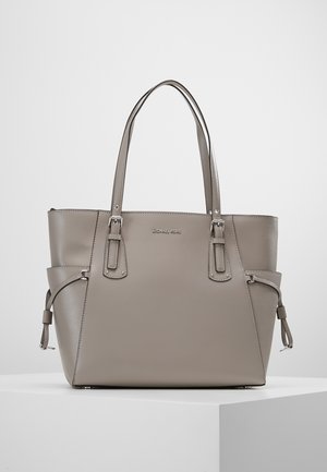 Taupe leather tote bag with double shoulder straps, side buckle details, and Michael Kors logo on the front, placed on a white surface.